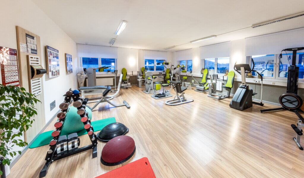 Modernes Fitnessstudio mit Trainingsgeräten, Hanteln und Übungsflächen.